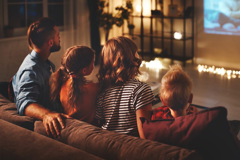 Family mother father and children watching projector, TV, movies with popcorn in evening at home.