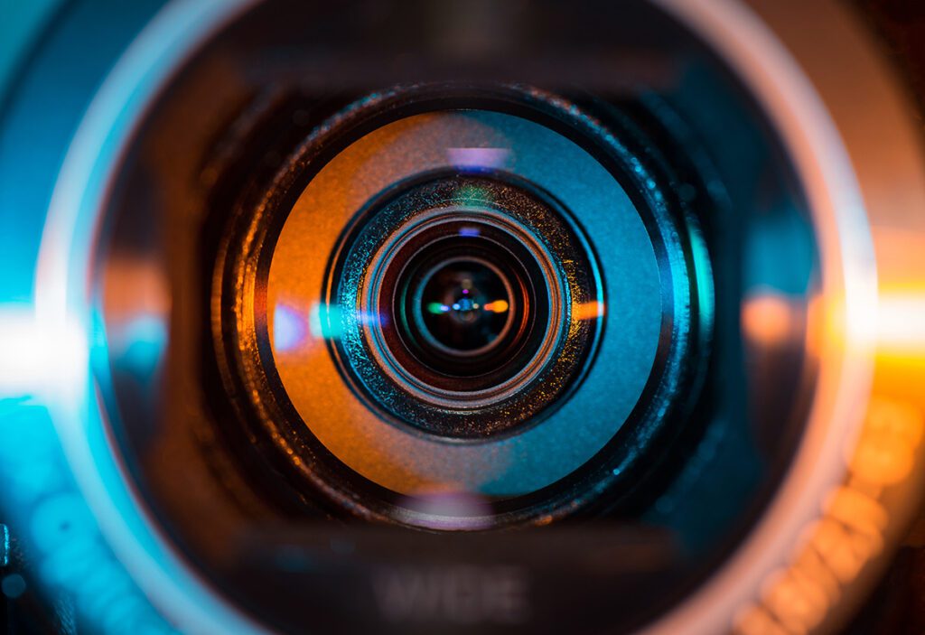 Video camera lens lit by blue and orange color light.